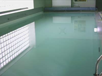 Hallenbad mit weißer Einhängefolie und Glasbaustein-Fenster, Wasserfläche spiegelt Deckenlicht