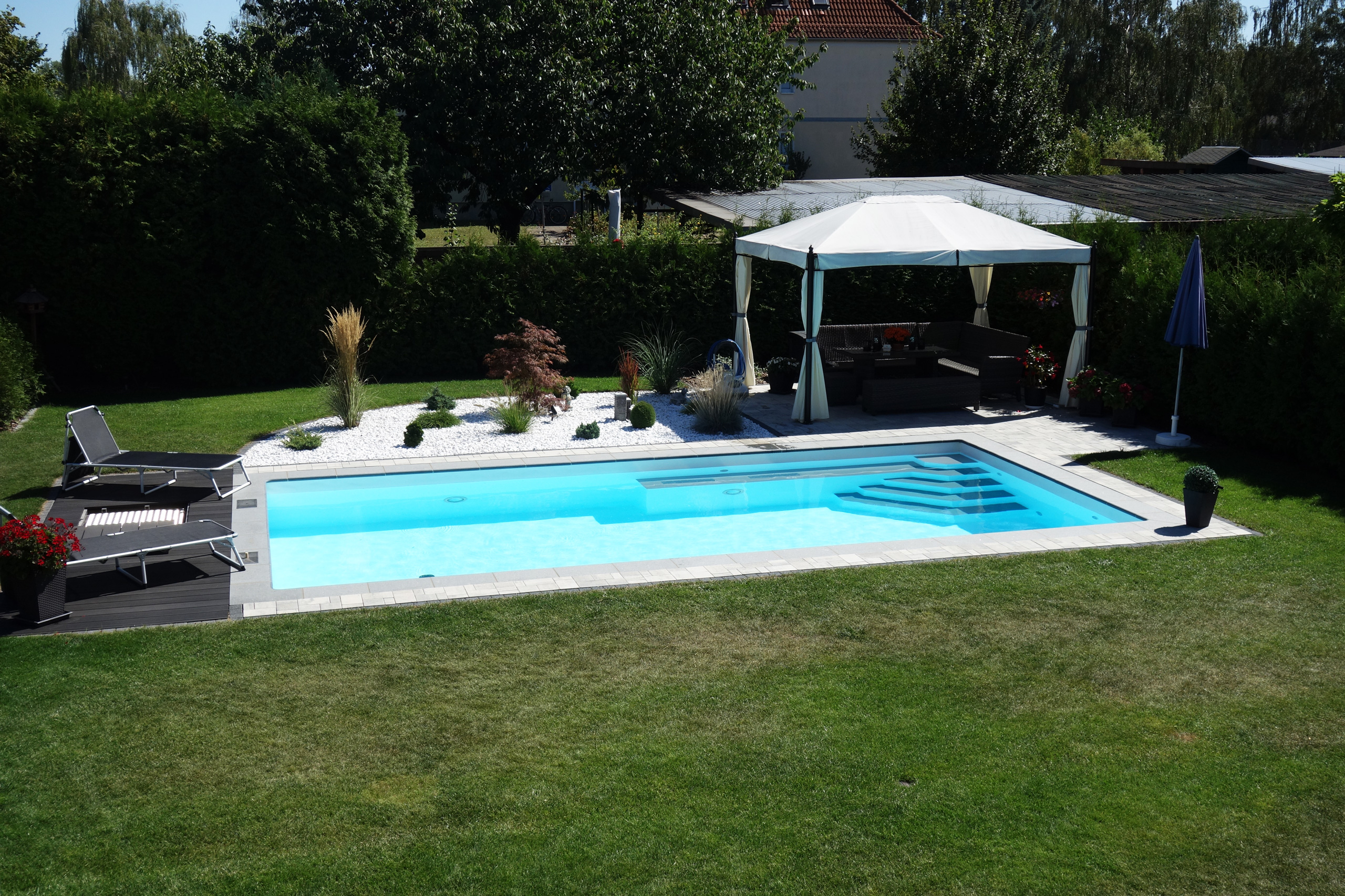 Gesamtaufnahme des Rechteckbeckens mit Ecktreppe, Podest und Luftsprudelsitz in einem Garten mit Pavillon.