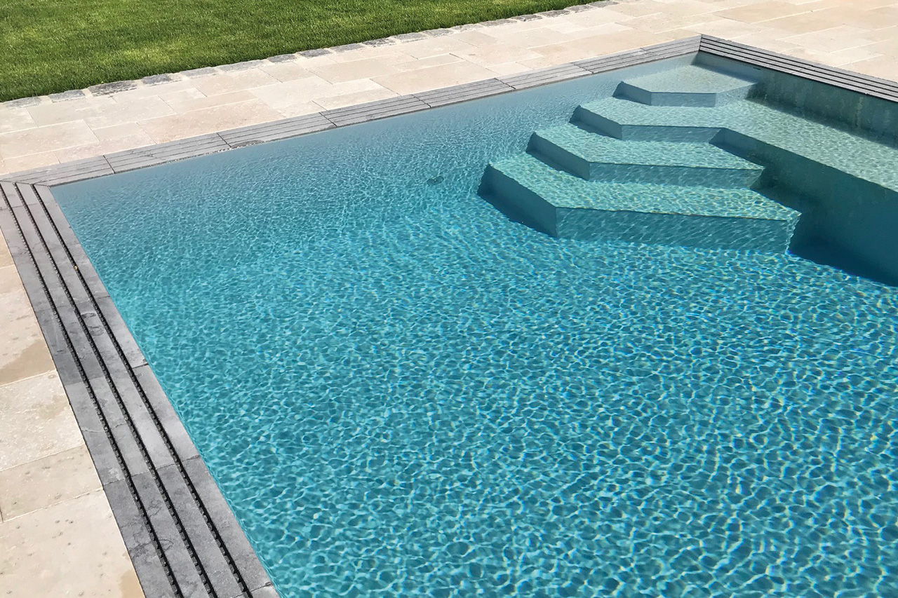 Überlaufbecken Overflow Stone EVO mit blauer Wasseroberfläche, Ecktreppe und Überlaufrinne