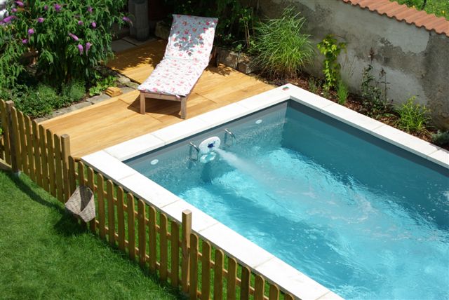 Gartenpool mit Gegenstromanlage und Holzterrasse, umgeben von Rasen und Zaun