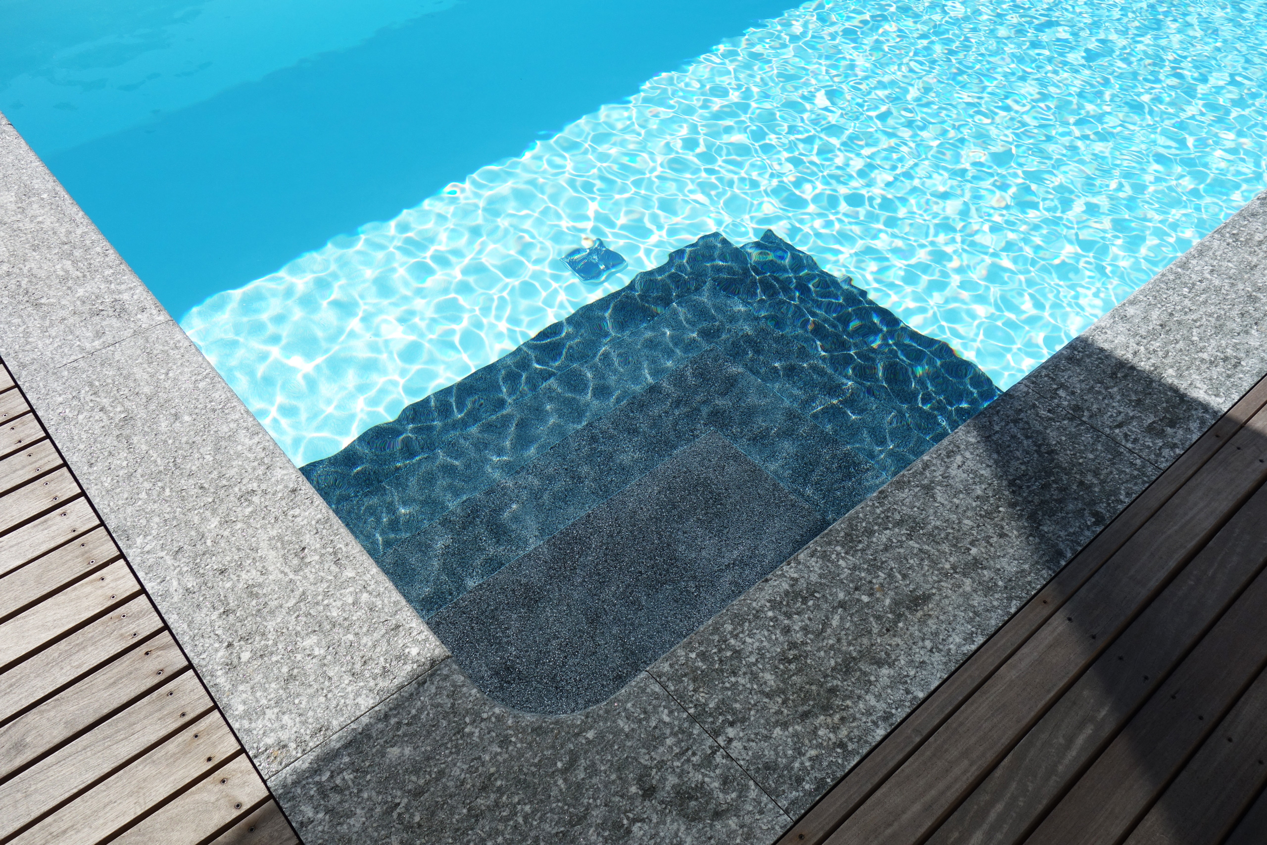 Ecktreppe und Podest eines Rechteckbeckens mit Unterflurabdeckung, umgeben von Holz- und Steinplatten