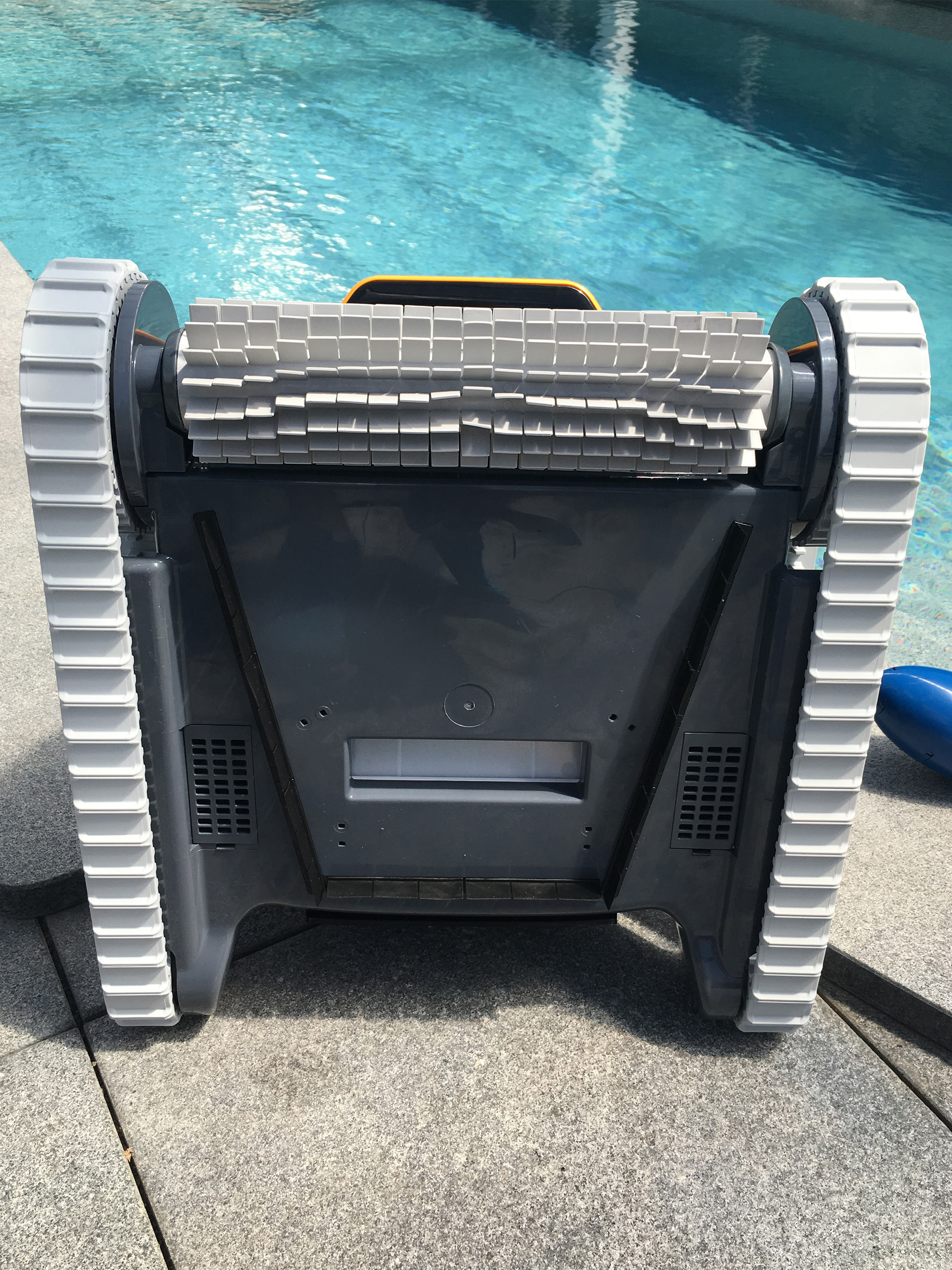 Unterseite des Poolroboters Dolphin E20 mit Bürsten und Raupenantrieb, vor einem blauen Pool