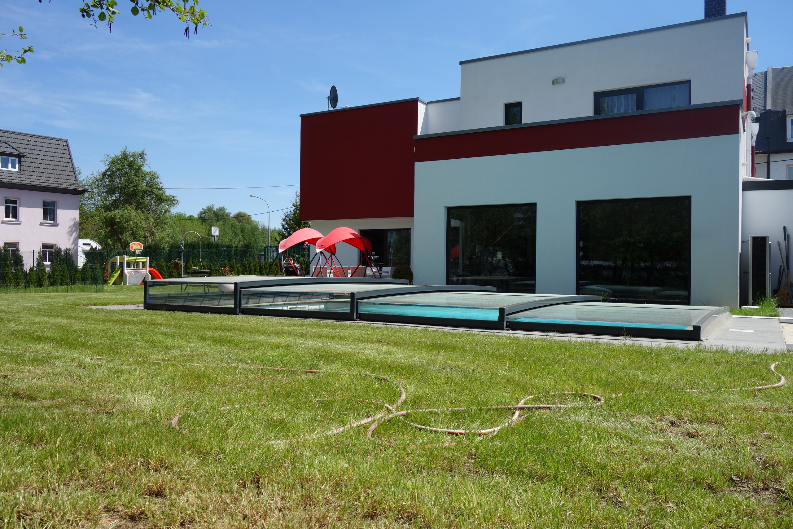 Betonbecken mit Überdachung Casablanca Infinity vor modernem Haus mit Rasenfläche und Garten