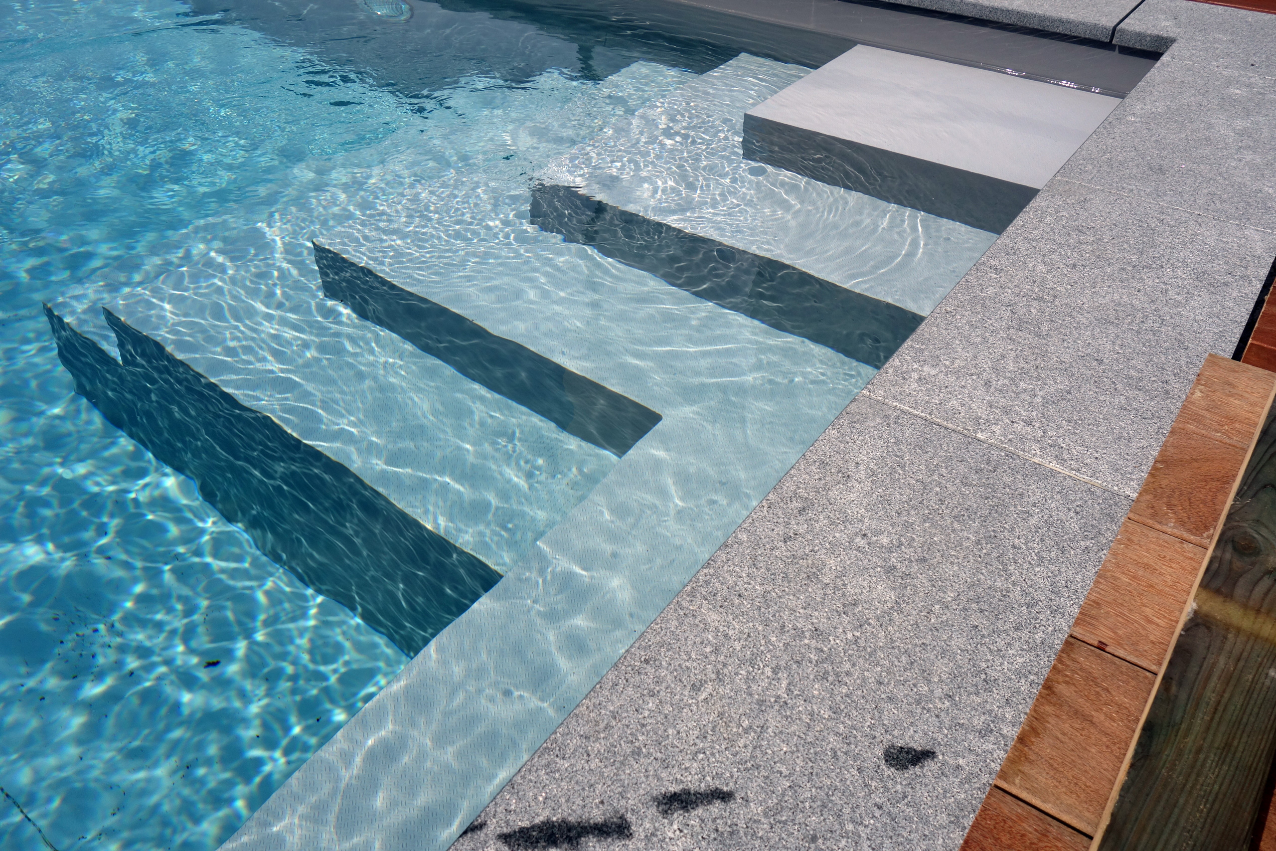 Detailansicht der hellgrauen Ecktreppe und des Podests im Betonbecken mit blauer Wasseroberfläche.