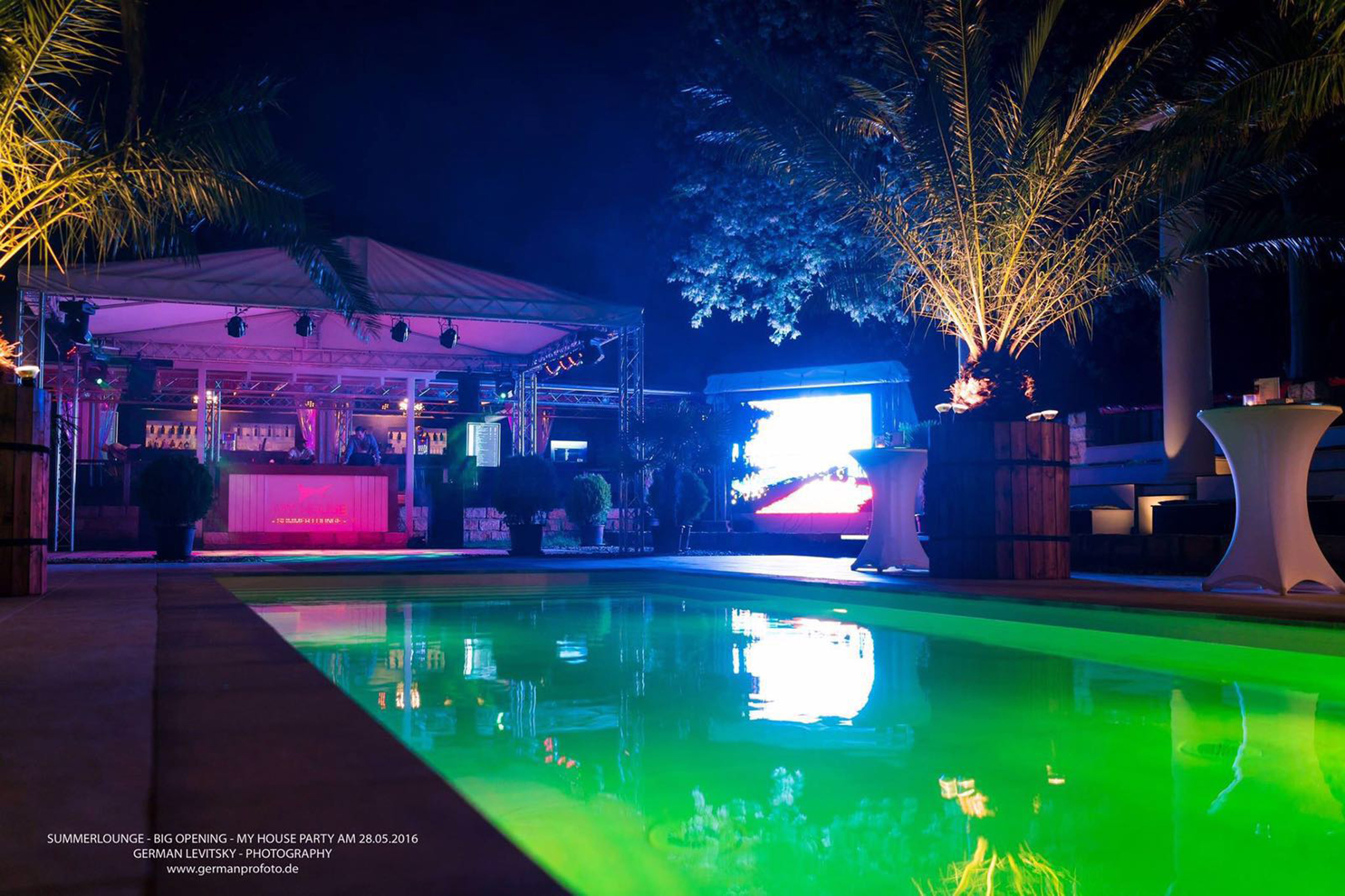 Schwimmbad 4x10x1,35m mit grüner Beleuchtung bei Nacht, umgeben von Palmen und einer Bar