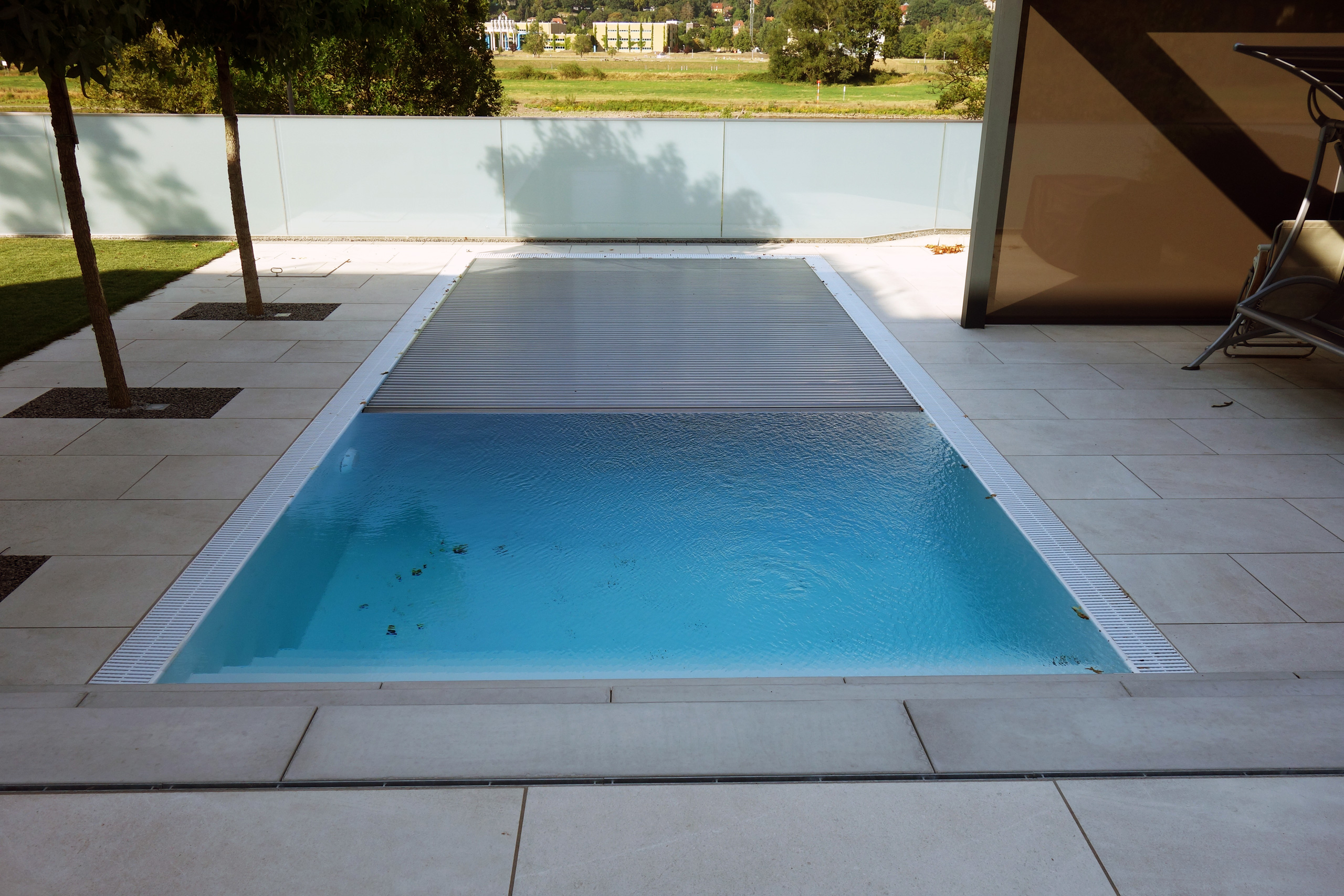 Überlaufpool mit Unterflurrolladen, teilweise geöffnet, um das blaue Wasser und die Überlaufrinne zu zeigen