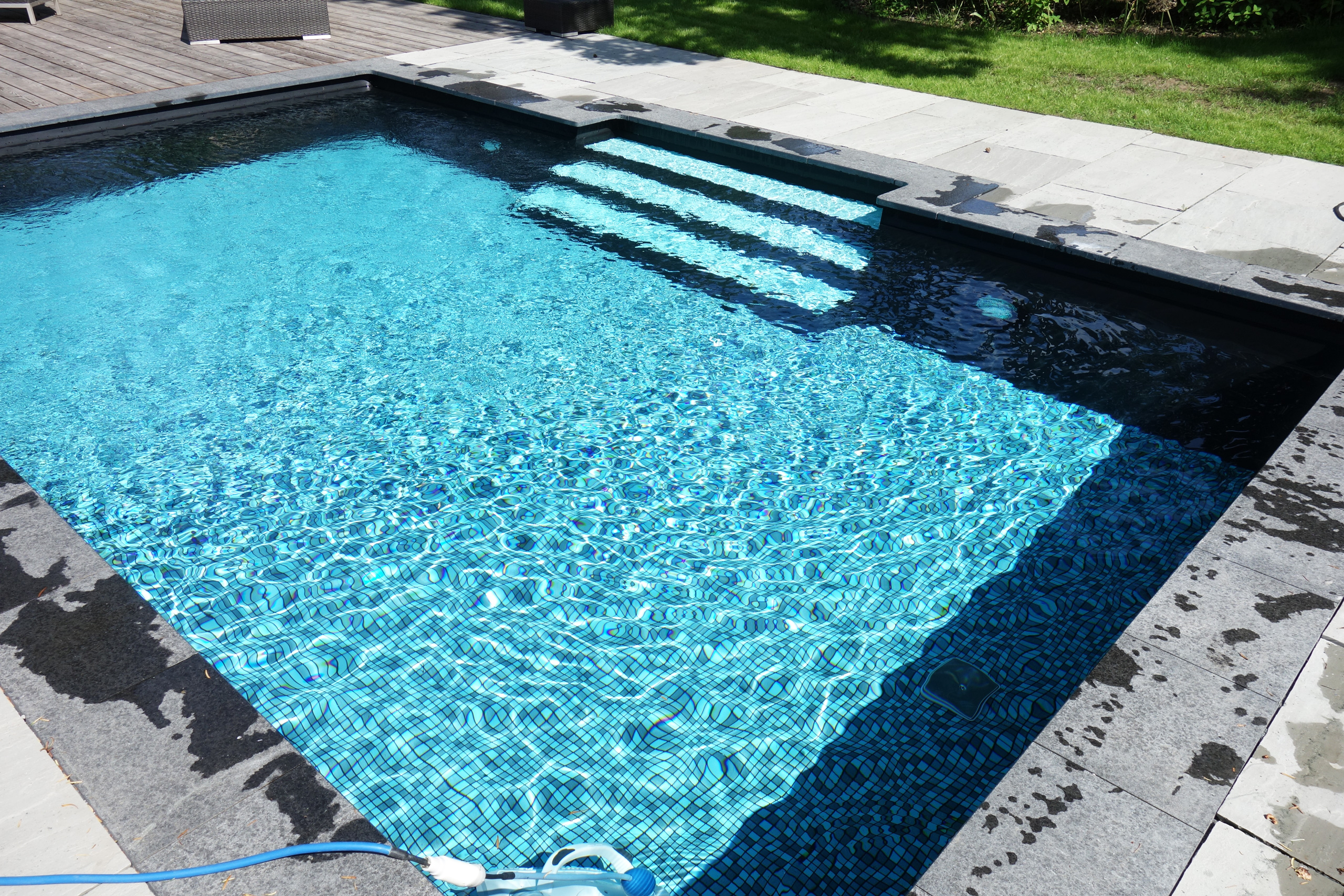 Blick auf den Rechteck-Pool mit gerader Treppe und blauer Folie, umgeben von grauen Steinplatten.