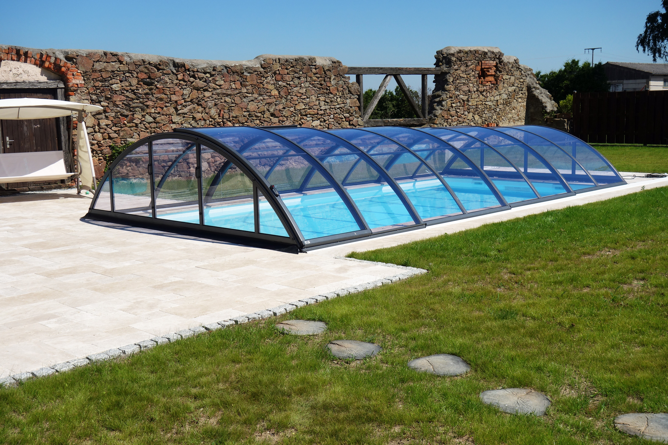 Schwimmbecken mit blauer Folie unter einer transparenten Poolüberdachung im Garten.