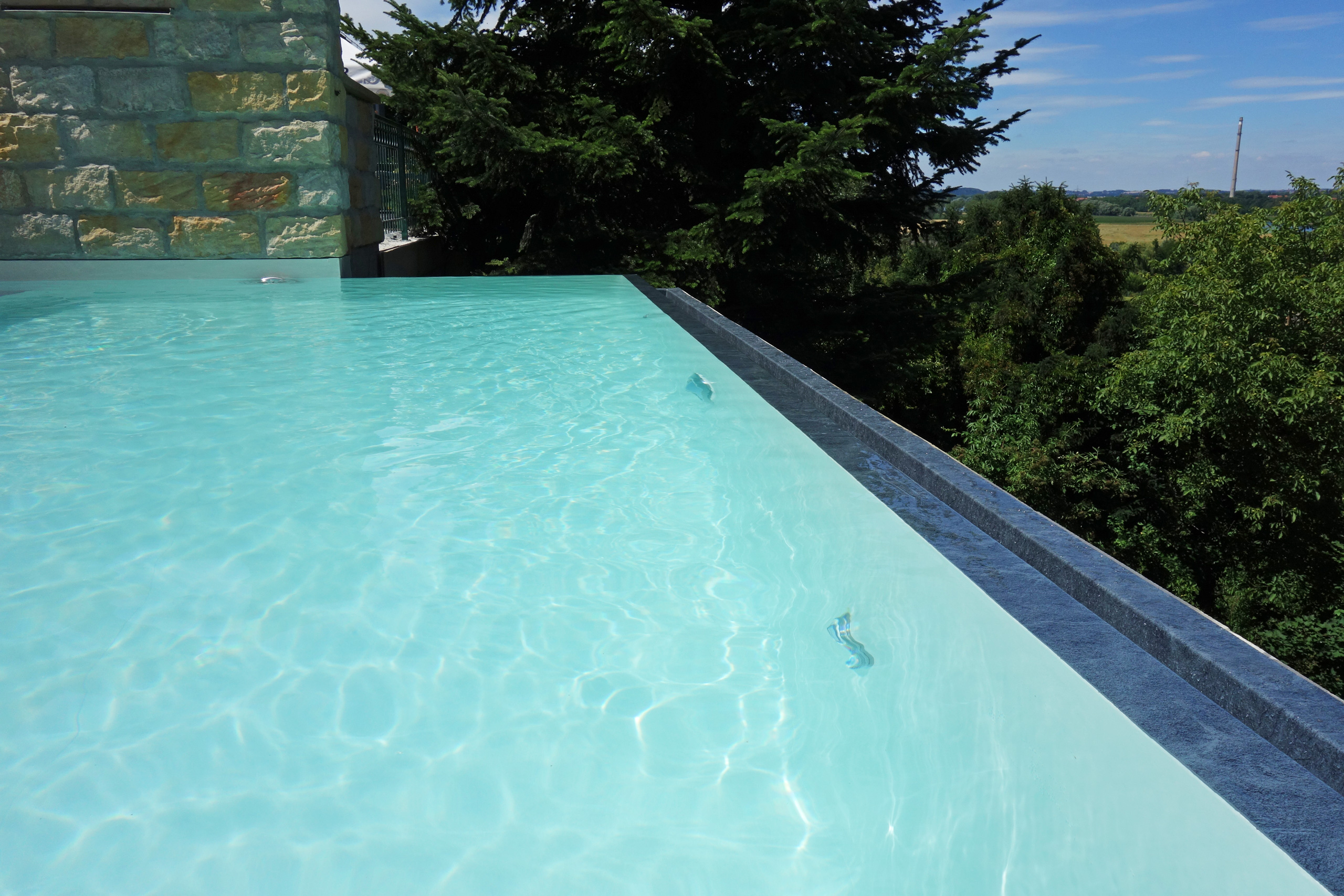 Überlaufbecken Infinity Pool mit blauem Wasser und Steinmauer im Hintergrund
