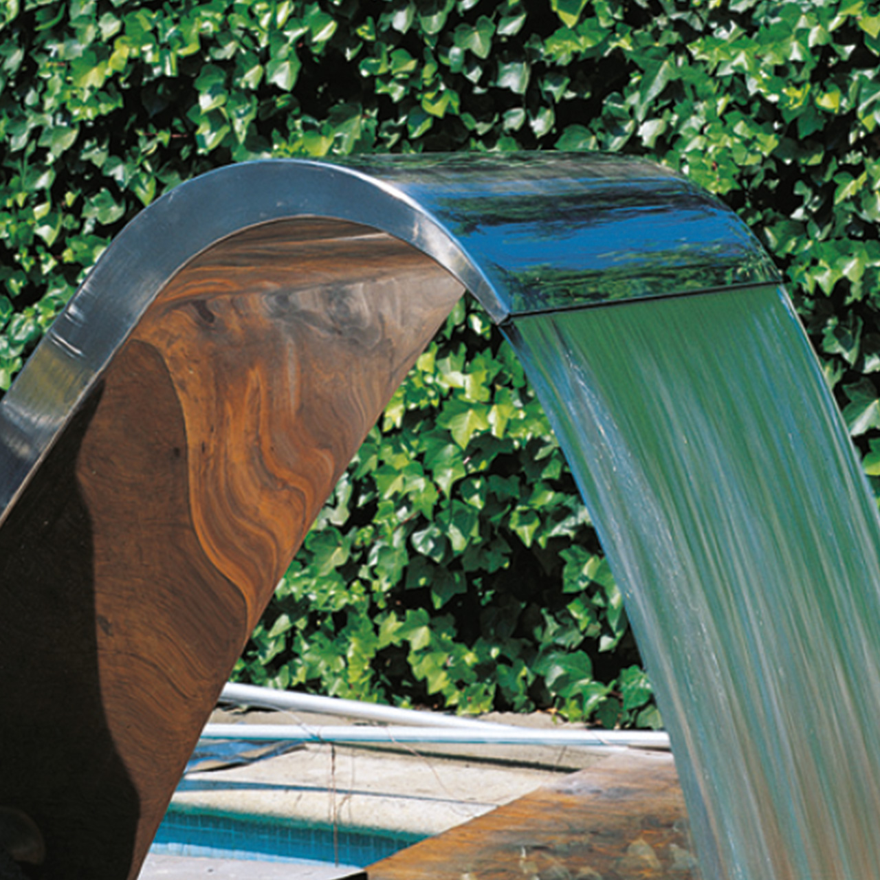 Detail der Schwalldusche Deluxe: breiter Wasserschwall aus glänzendem Edelstahl, kombiniert mit rostbraunem Sockel.