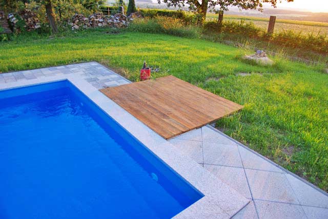 Rechteckbecken mit blauer Einhängefolie, umgeben von hellen Platten und einer Holzterrasse