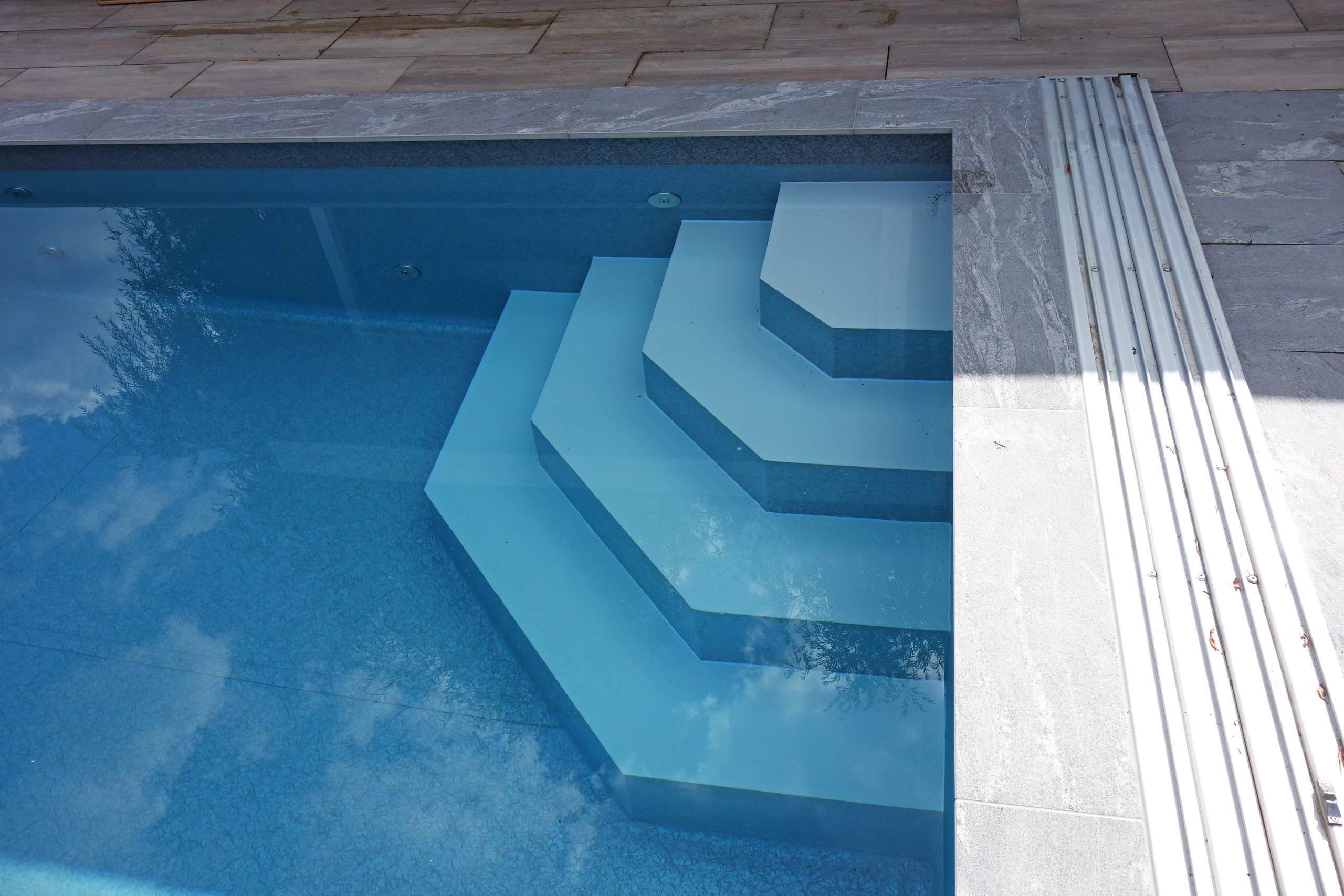 Ecktreppe und Podest im Schwimmbecken mit blauer Folie, daneben die Poolabdeckung