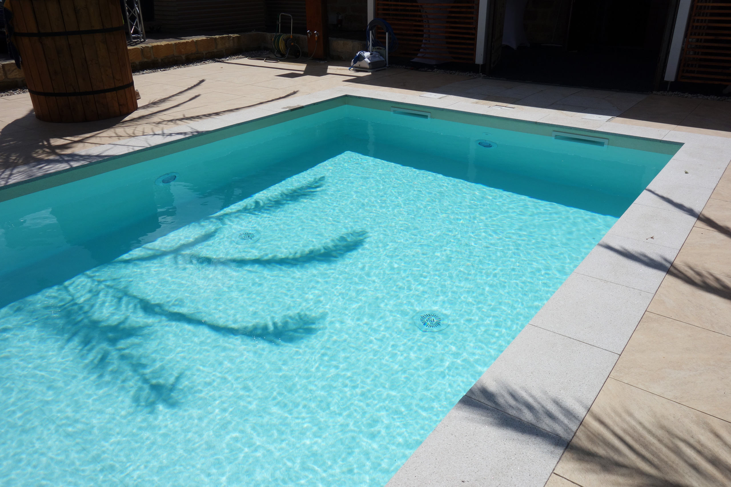 Blick auf das Schwimmbad mit gerader Treppe und Podest, umgeben von hellen Poolrandplatten.