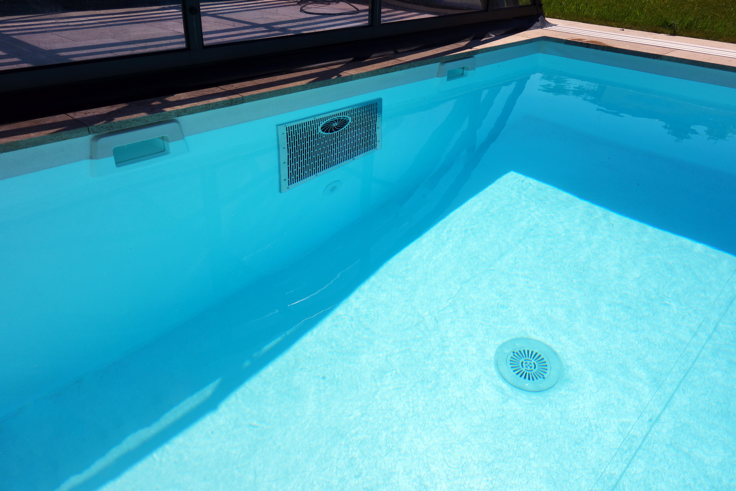 Detailansicht eines Schwimmbeckens mit Strömungsturbine, Einlaufdüse und Bodenablauf im hellblauen Wasser.