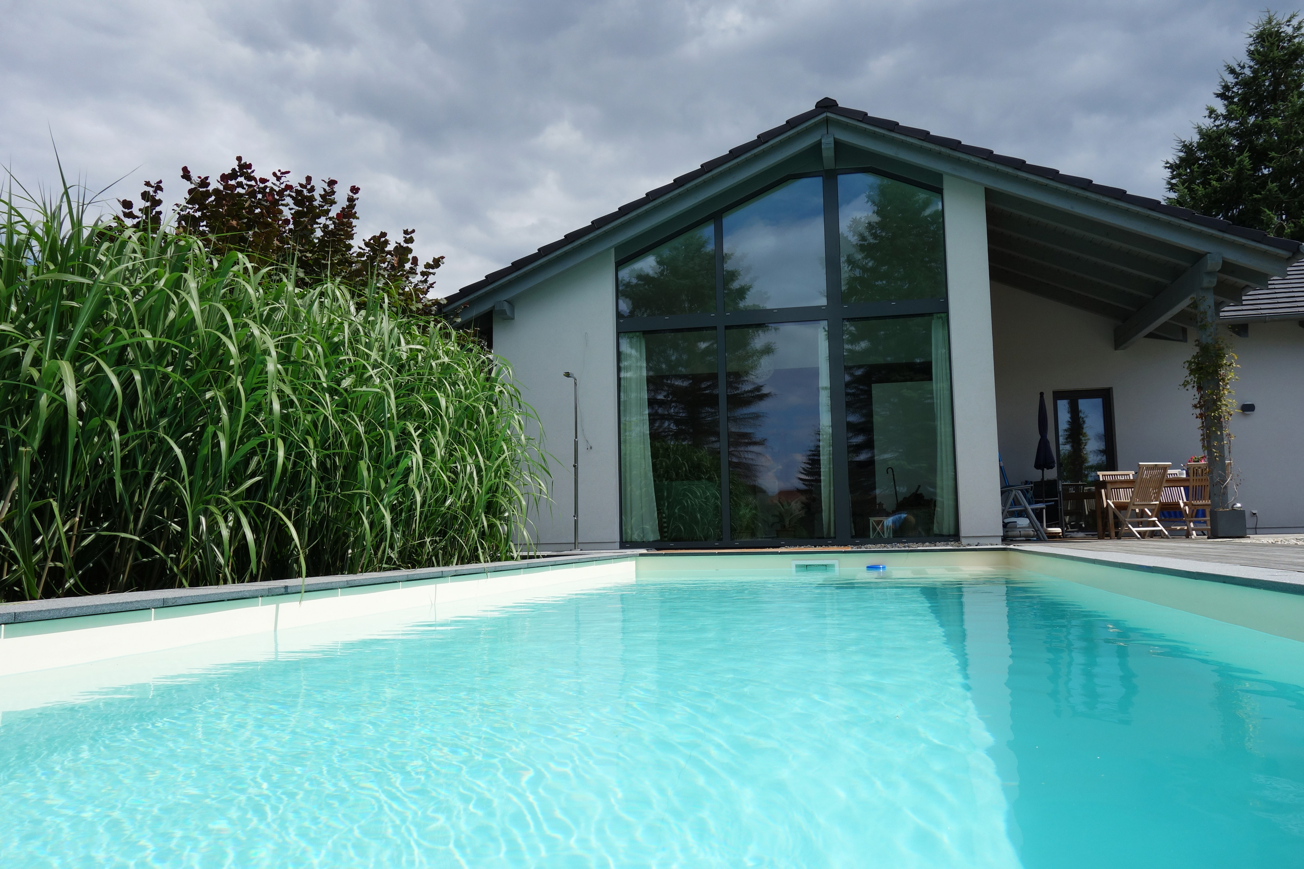 Blick über die Wasseroberfläche eines herausstehenden Swimmingpools mit Ecktreppe zum modernen Wohnhaus.