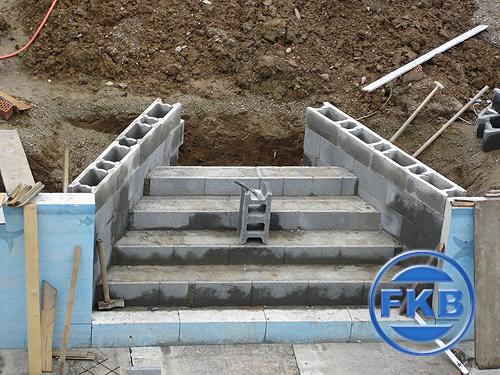 Rohbau einer gemauerten Treppe für die Beckensanierung, umgeben von Erdaushub und Baumaterialien.