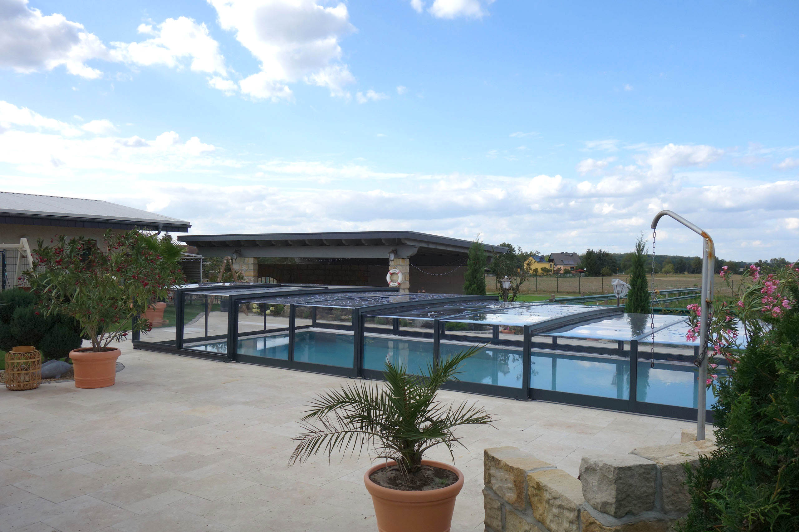 Poolüberdachung Prestige Plus mit transparenten Segmenten über einem blauen Pool im Garten