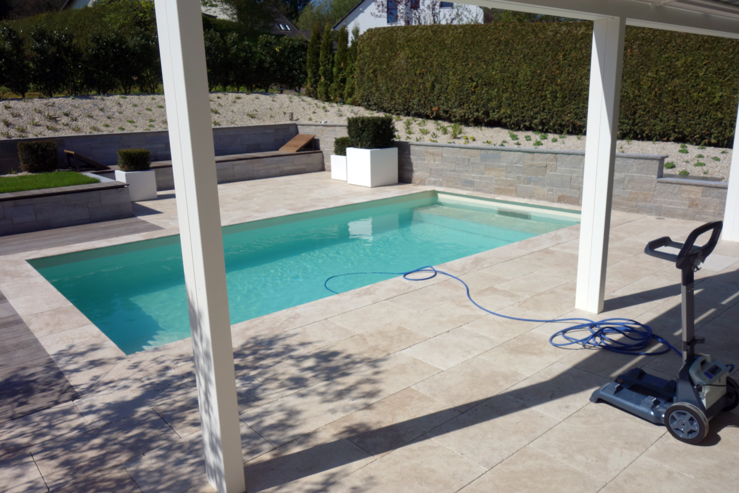 Schwimmbecken mit blauer Poolfolie und blauer Schwimmbadschlauch auf beigem Terrassenboden