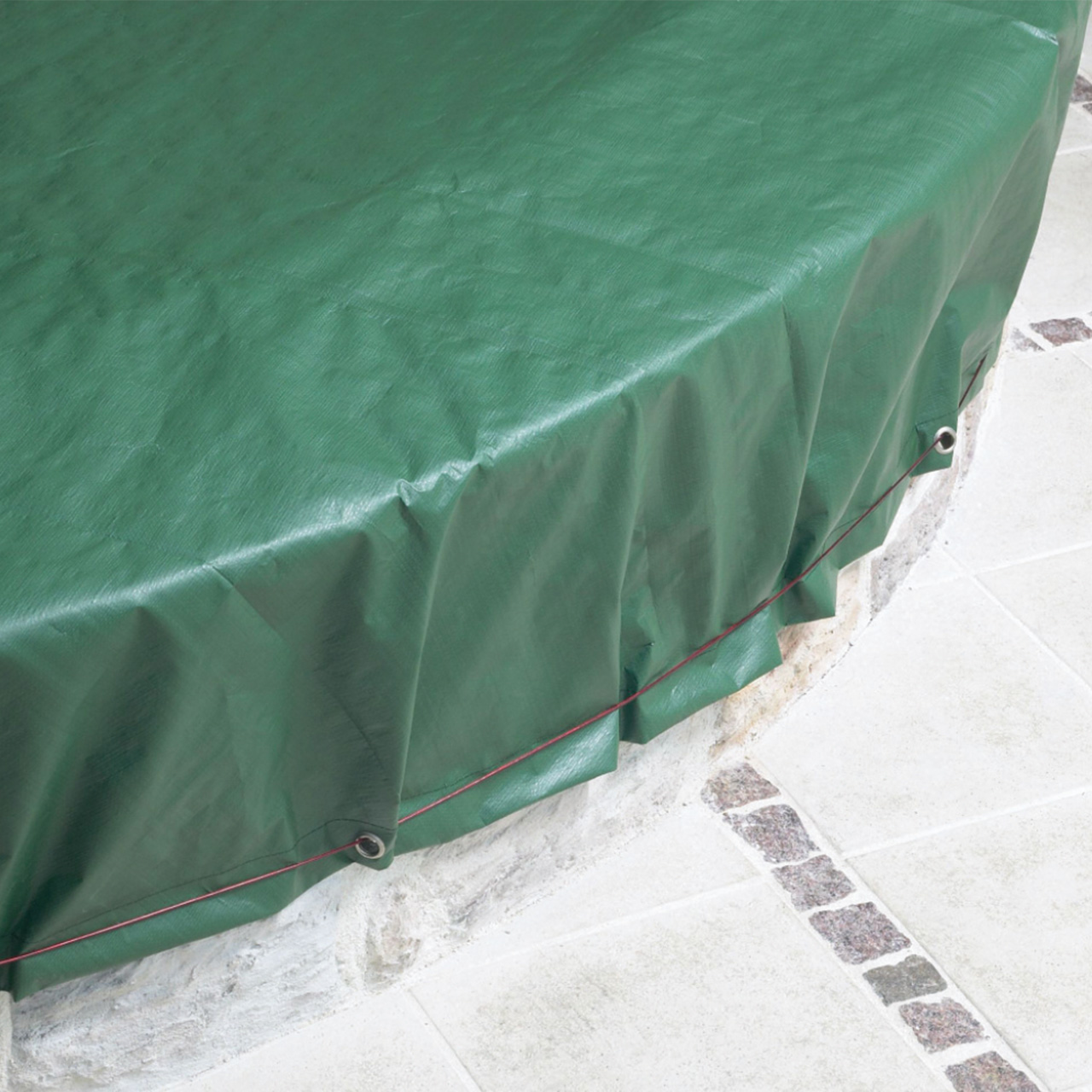 Grüne Abdeckplane für Rundbecken mit Ösen und Spannseil, das über einen gemauerten Beckenrand verläuft.