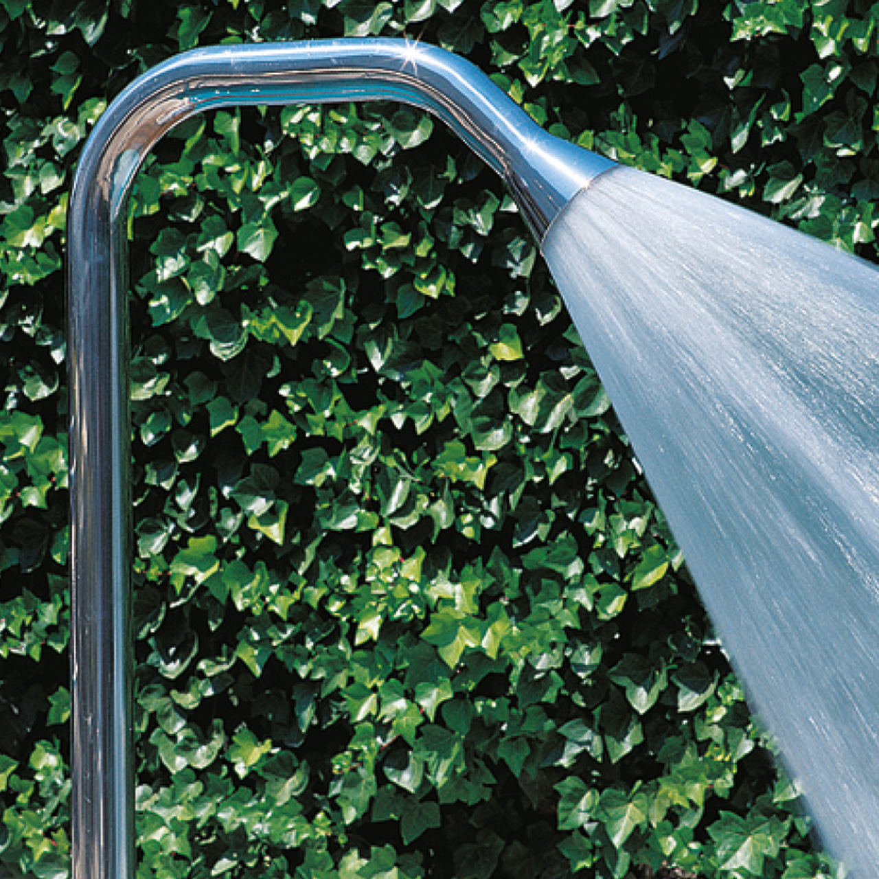 Glockendusche aus Edelstahl mit Wasserstrahl vor grüner Hecke
