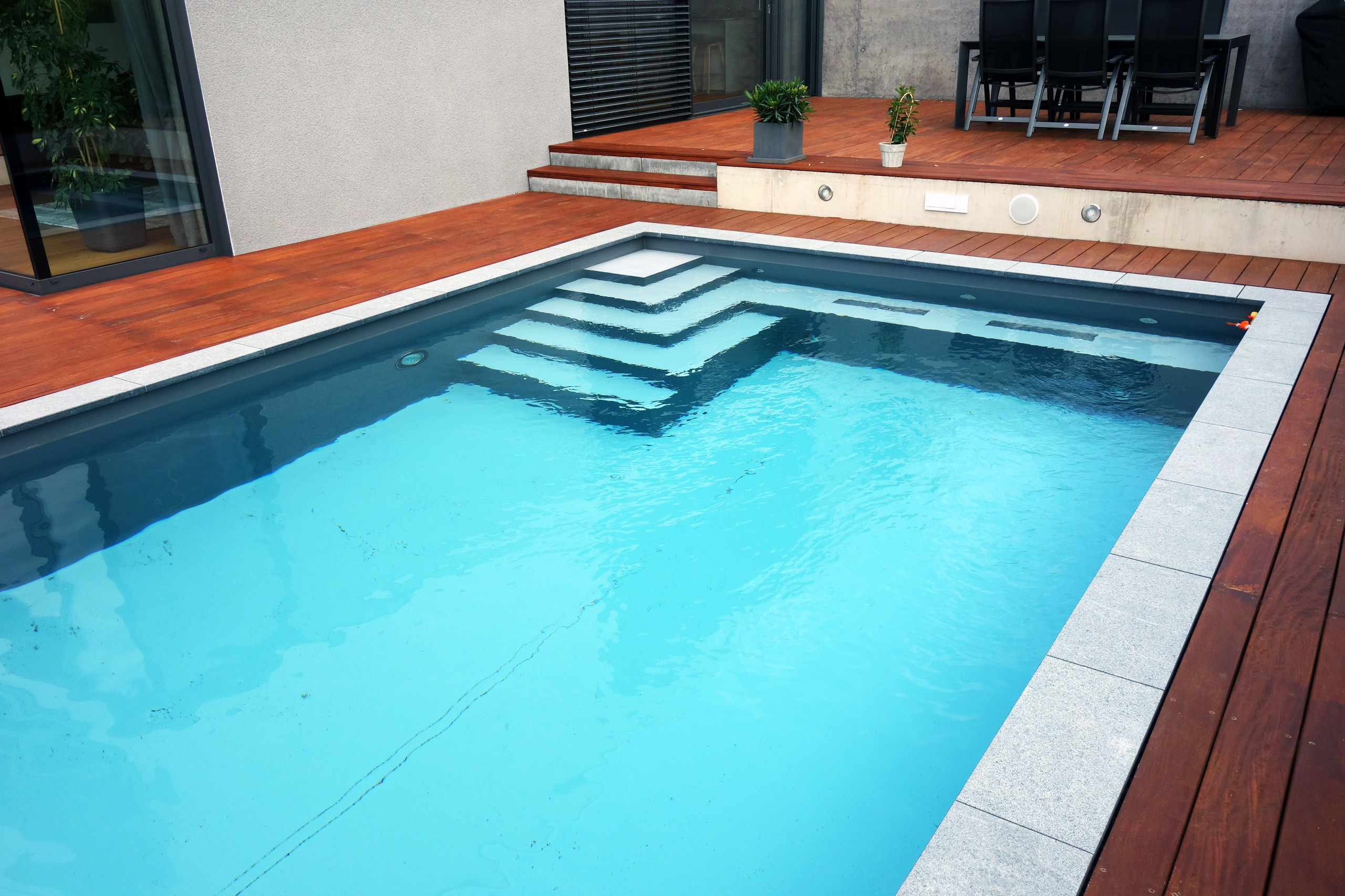 Betonbecken 3,5x7x1,5m mit Ecktreppe und Podest, umgeben von Holzterrasse und Steinplatten