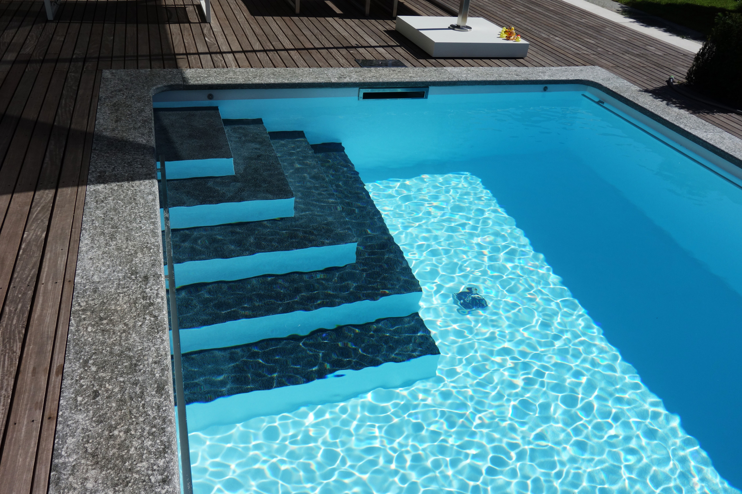 Blick auf die Ecktreppe und das Podest eines Rechteckbeckens mit Unterflurabdeckung und blauer Folie.